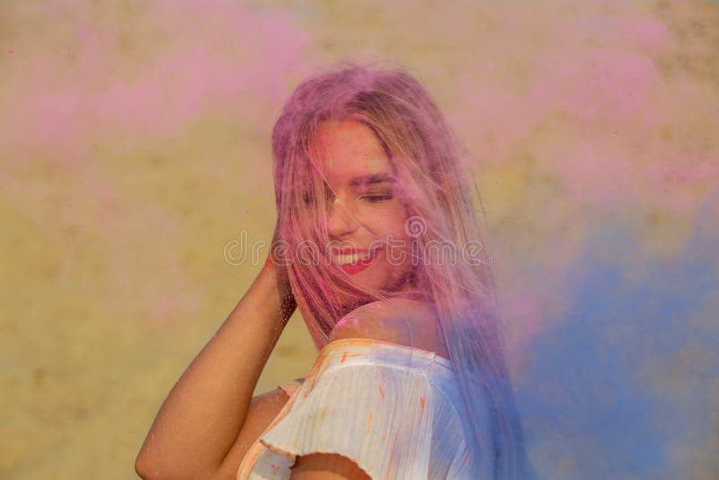 Cheerful blonde woman playing with pink and blue dry paint Holi. Cheerful blonde model playing with pink and blue dry paint Holi at the desert stock image
